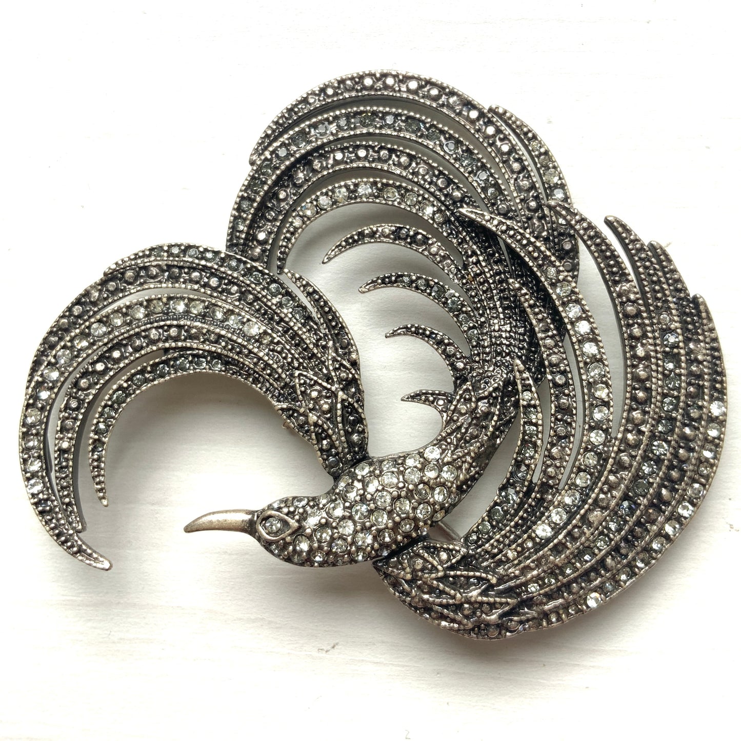 A vintage bird brooch in silver-tone metal, defined by its flowing, sculptural lines. 流れるようなラインが印象的な、鳥モチーフのブローチ。
