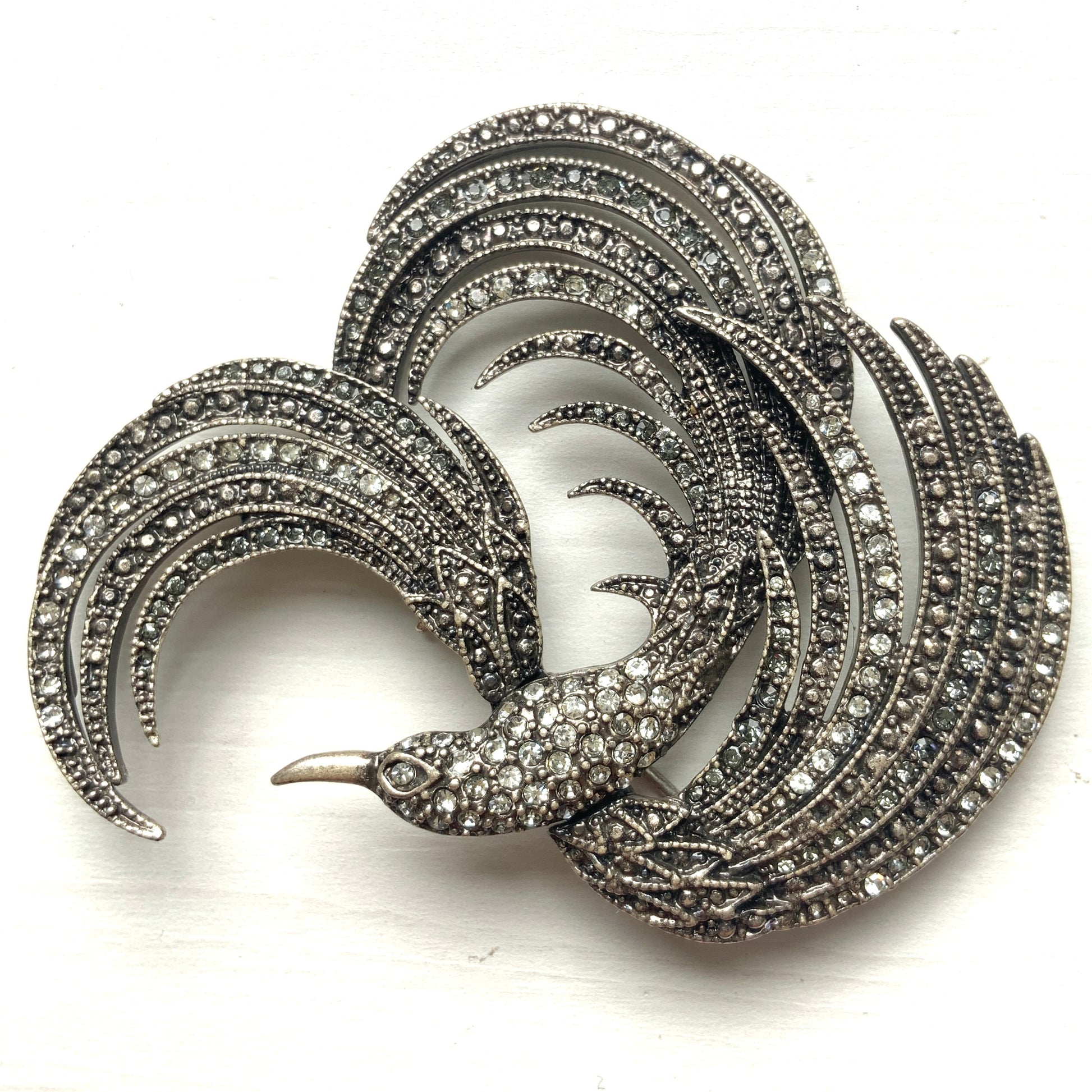 A vintage bird brooch in silver-tone metal, defined by its flowing, sculptural lines. 流れるようなラインが印象的な、鳥モチーフのブローチ。