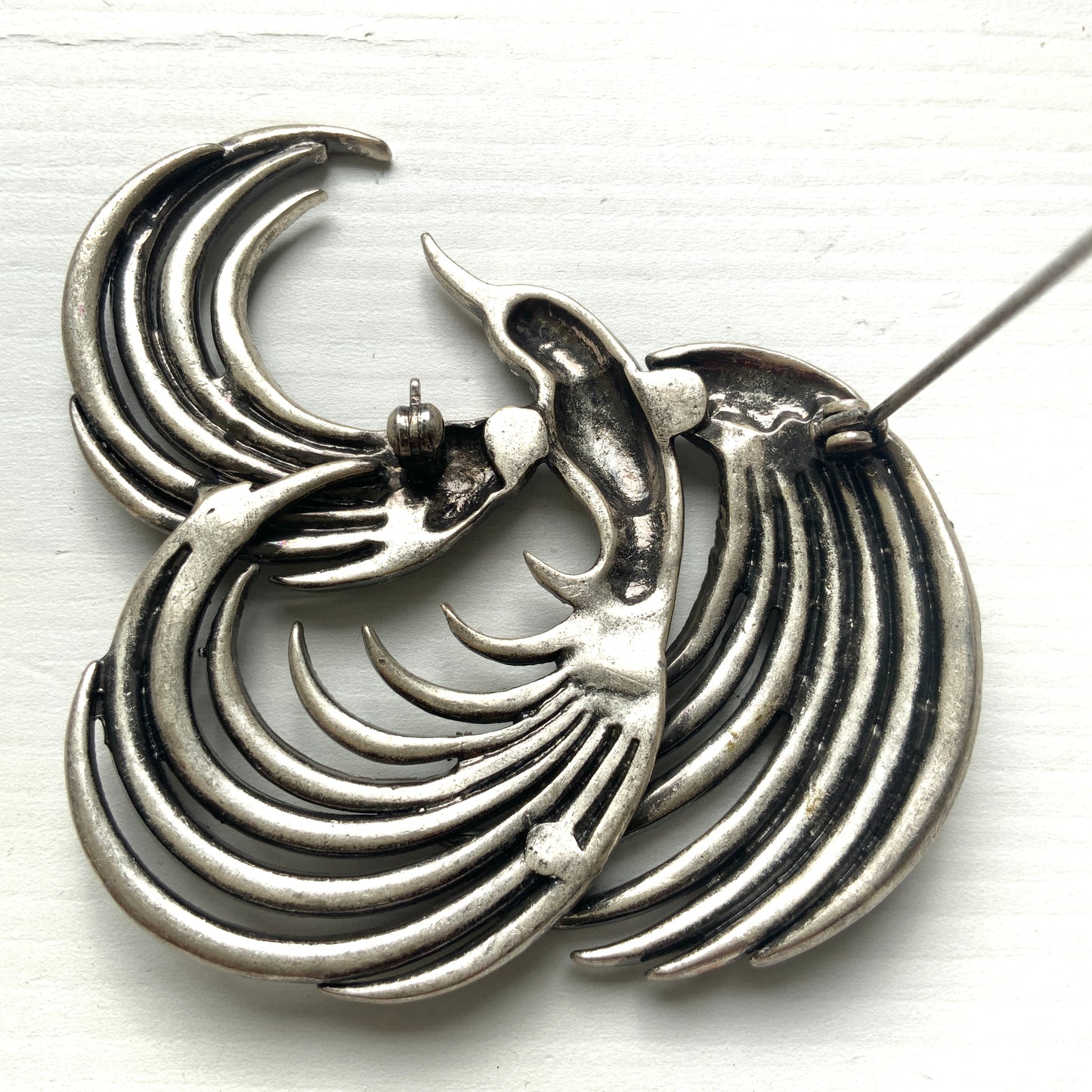 A vintage bird brooch in silver-tone metal, defined by its flowing, sculptural lines. 流れるようなラインが印象的な、鳥モチーフのブローチ。