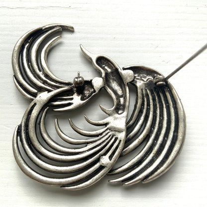 A vintage bird brooch in silver-tone metal, defined by its flowing, sculptural lines. 流れるようなラインが印象的な、鳥モチーフのブローチ。