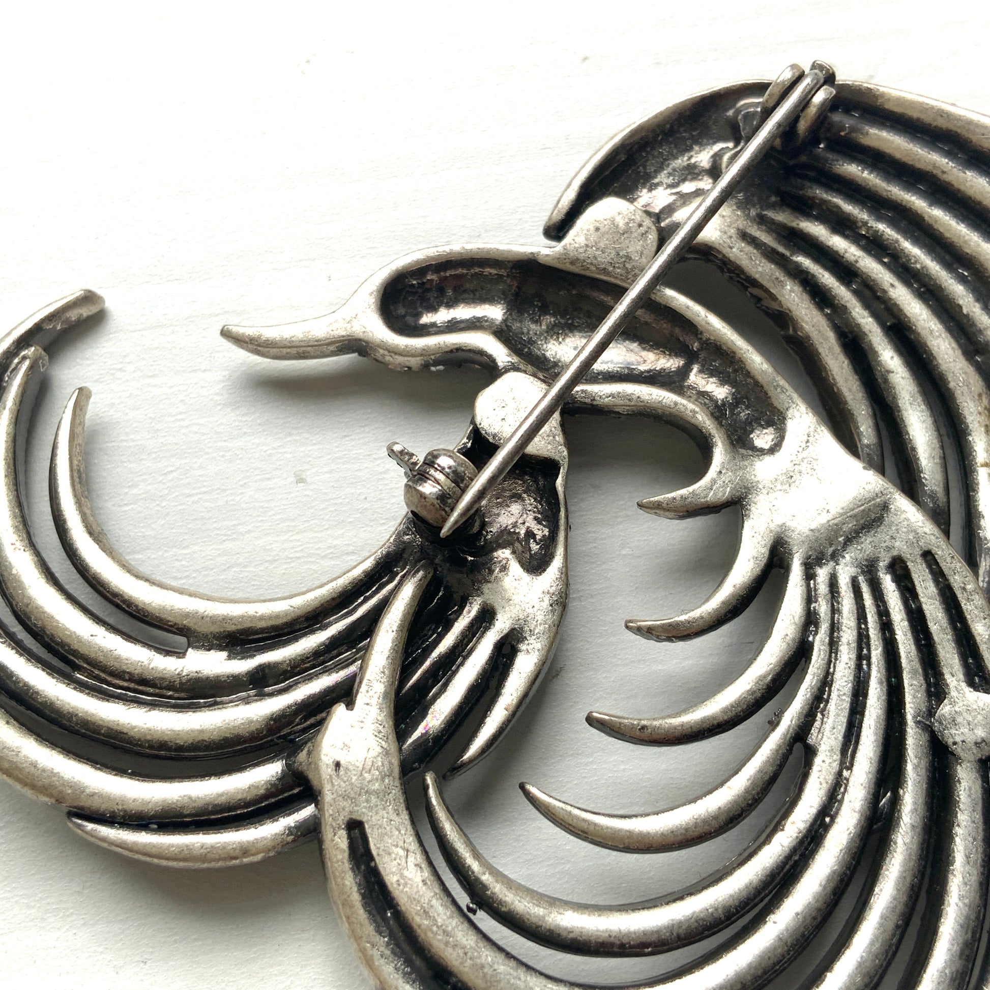 A vintage bird brooch in silver-tone metal, defined by its flowing, sculptural lines. 流れるようなラインが印象的な、鳥モチーフのブローチ。