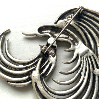 A vintage bird brooch in silver-tone metal, defined by its flowing, sculptural lines. 流れるようなラインが印象的な、鳥モチーフのブローチ。