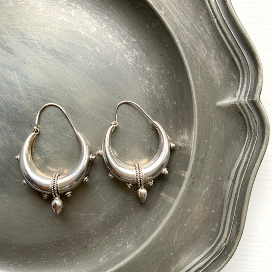 Bold silver hoop earrings in a crescent form, decorated with granulated details and teardrop-shaped protrusions. 三日月型に粒状の装飾とドロップ状の突起をあしらった存在感のあるシルバーフープピアス。 