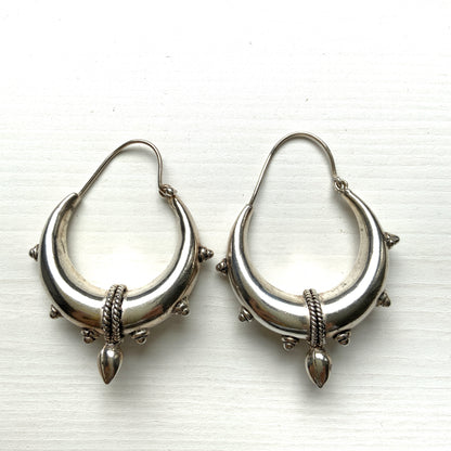 Bold silver hoop earrings in a crescent form, decorated with granulated details and teardrop-shaped protrusions. 三日月型に粒状の装飾とドロップ状の突起をあしらった存在感のあるシルバーフープピアス。 
