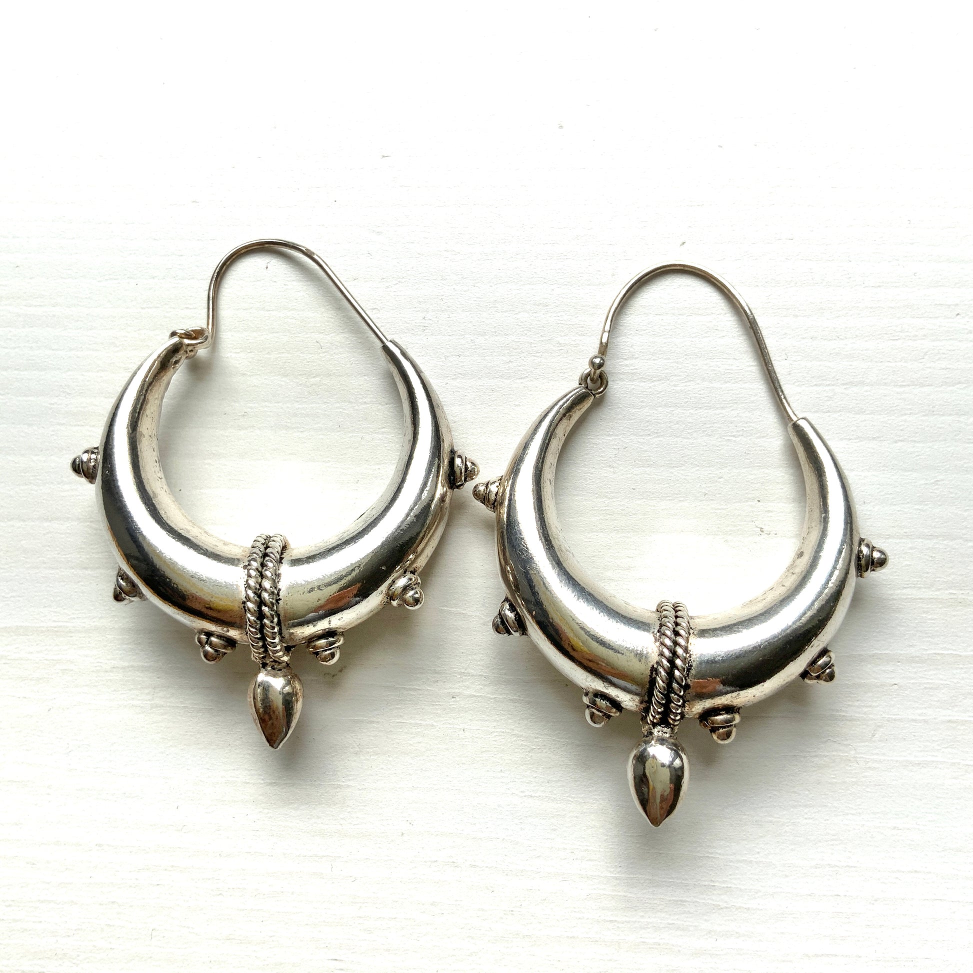 Bold silver hoop earrings in a crescent form, decorated with granulated details and teardrop-shaped protrusions. 三日月型に粒状の装飾とドロップ状の突起をあしらった存在感のあるシルバーフープピアス。 