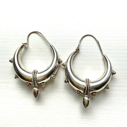 Bold silver hoop earrings in a crescent form, decorated with granulated details and teardrop-shaped protrusions. 三日月型に粒状の装飾とドロップ状の突起をあしらった存在感のあるシルバーフープピアス。 