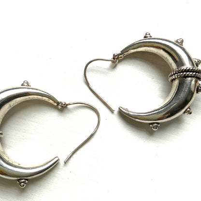 Bold silver hoop earrings in a crescent form, decorated with granulated details and teardrop-shaped protrusions. 三日月型に粒状の装飾とドロップ状の突起をあしらった存在感のあるシルバーフープピアス。 