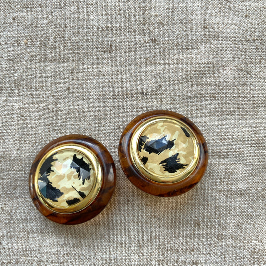 Dome-shaped clip-on earrings featuring a striking art pattern reminiscent of camouflage, framed in a faux tortoiseshell rim. べっ甲風の縁に、迷彩のようなアートパターンが印象的なドーム型イヤリング。