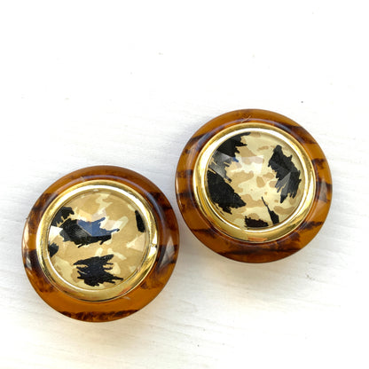 Dome-shaped clip-on earrings featuring a striking art pattern reminiscent of camouflage, framed in a faux tortoiseshell rim. べっ甲風の縁に、迷彩のようなアートパターンが印象的なドーム型イヤリング。