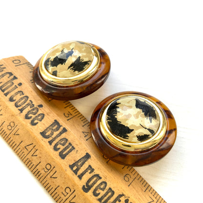 Dome-shaped clip-on earrings featuring a striking art pattern reminiscent of camouflage, framed in a faux tortoiseshell rim. べっ甲風の縁に、迷彩のようなアートパターンが印象的なドーム型イヤリング。