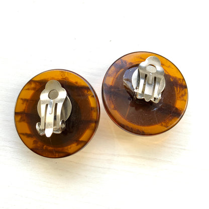 Dome-shaped clip-on earrings featuring a striking art pattern reminiscent of camouflage, framed in a faux tortoiseshell rim. べっ甲風の縁に、迷彩のようなアートパターンが印象的なドーム型イヤリング。