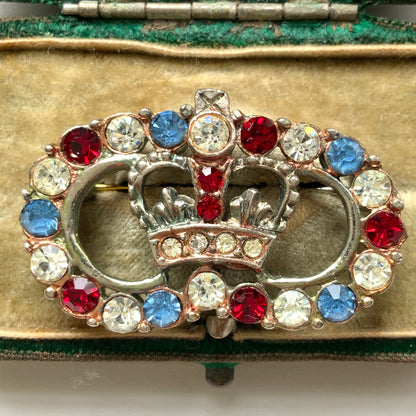 A brooch featuring a crown encircled by tricolour rhinestones – red, clear and blue. 王冠の周りをトリコロールカラーのラインストーンが囲んだブローチ。