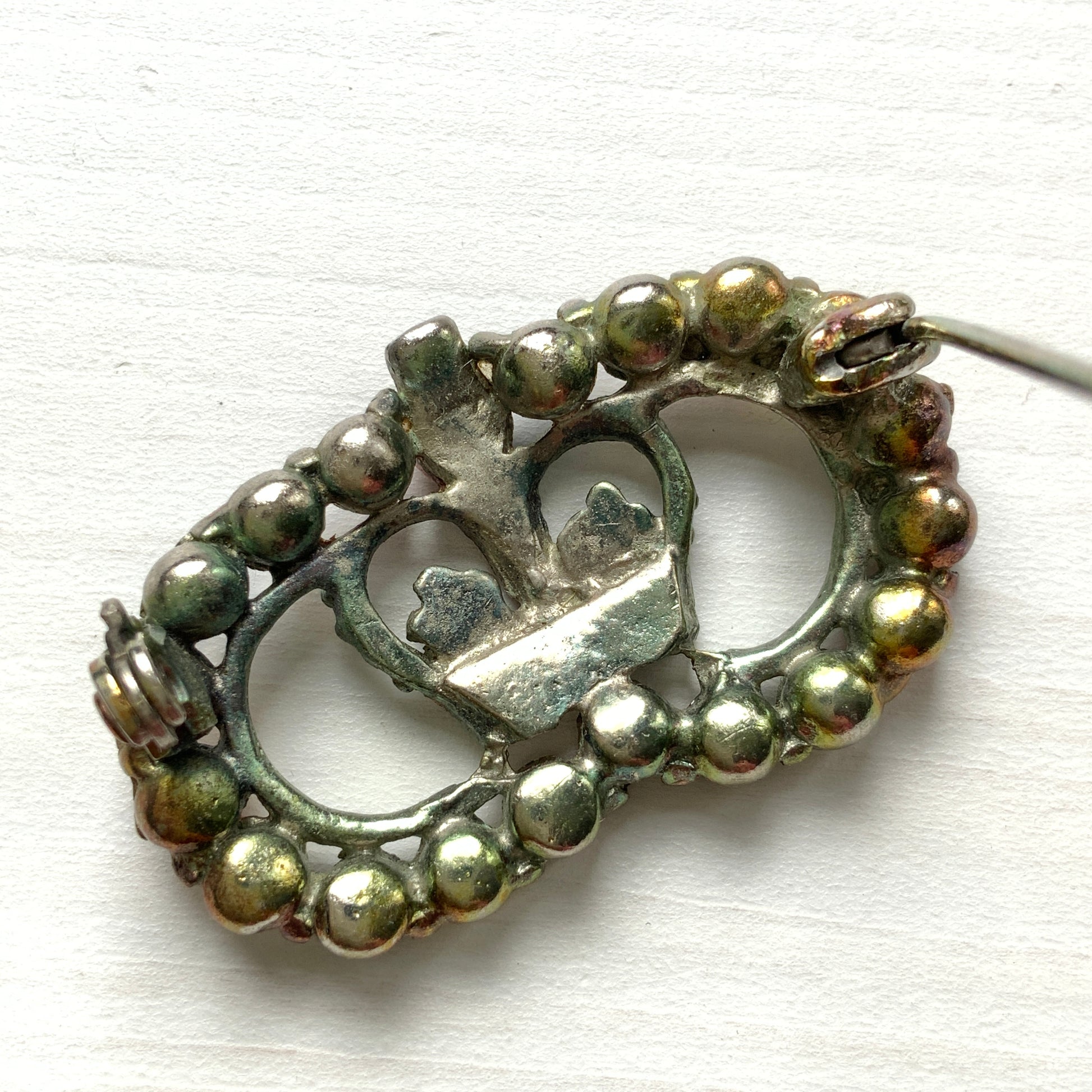 A brooch featuring a crown encircled by tricolour rhinestones – red, clear and blue. 王冠の周りをトリコロールカラーのラインストーンが囲んだブローチ。