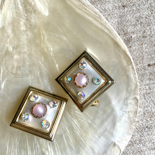 Clip-on earrings featuring white square plastic made to resemble mother of pearl, accented with pink plastic cabochons and shimmering aurora borealis stones. マザーオブパールを模したホワイトのスクエアプラスチックに、ピンクのプラスチックカボションとオーロラストーンが輝くクリップイヤリング。