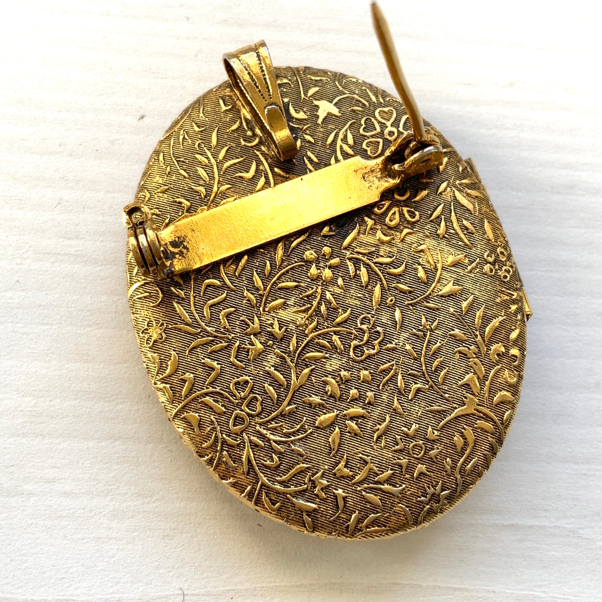 A gold-tone locket brooch featuring a floral motif accented with turquoise blue cabochons.  ゴールドトーンのお花に、ターコイズブルーのカボションが映えるロケットブローチ。