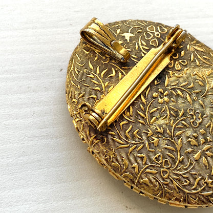 A gold-tone locket brooch featuring a floral motif accented with turquoise blue cabochons.  ゴールドトーンのお花に、ターコイズブルーのカボションが映えるロケットブローチ。