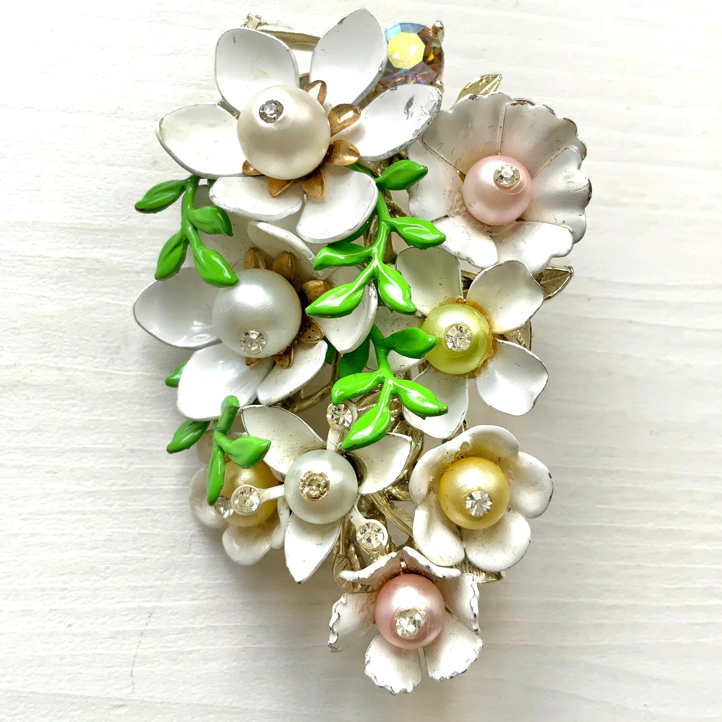 Vintage 1950s brooch featuring white enamel flowers adorned with soft pastel-coloured pearls. ホワイトエナメルの花に淡いパステルカラーのパールがあしらわれた、1950年代のヴィンテージブローチ。